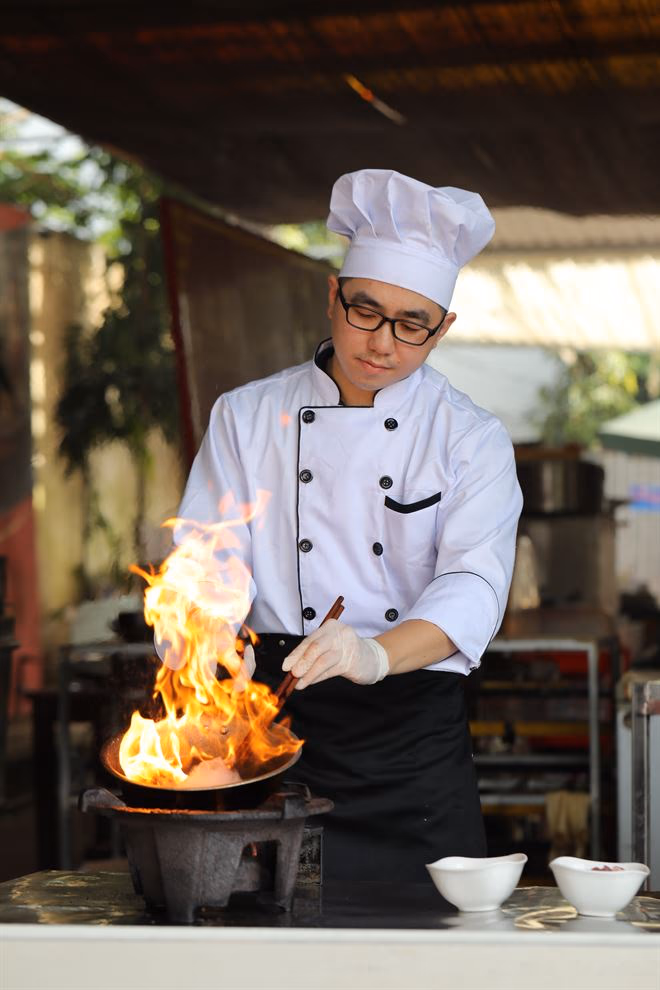 Nguyễn Tiến Hải trong bộ đồ bếp trưởng, nướng gừng và hành trên lửa lớn.